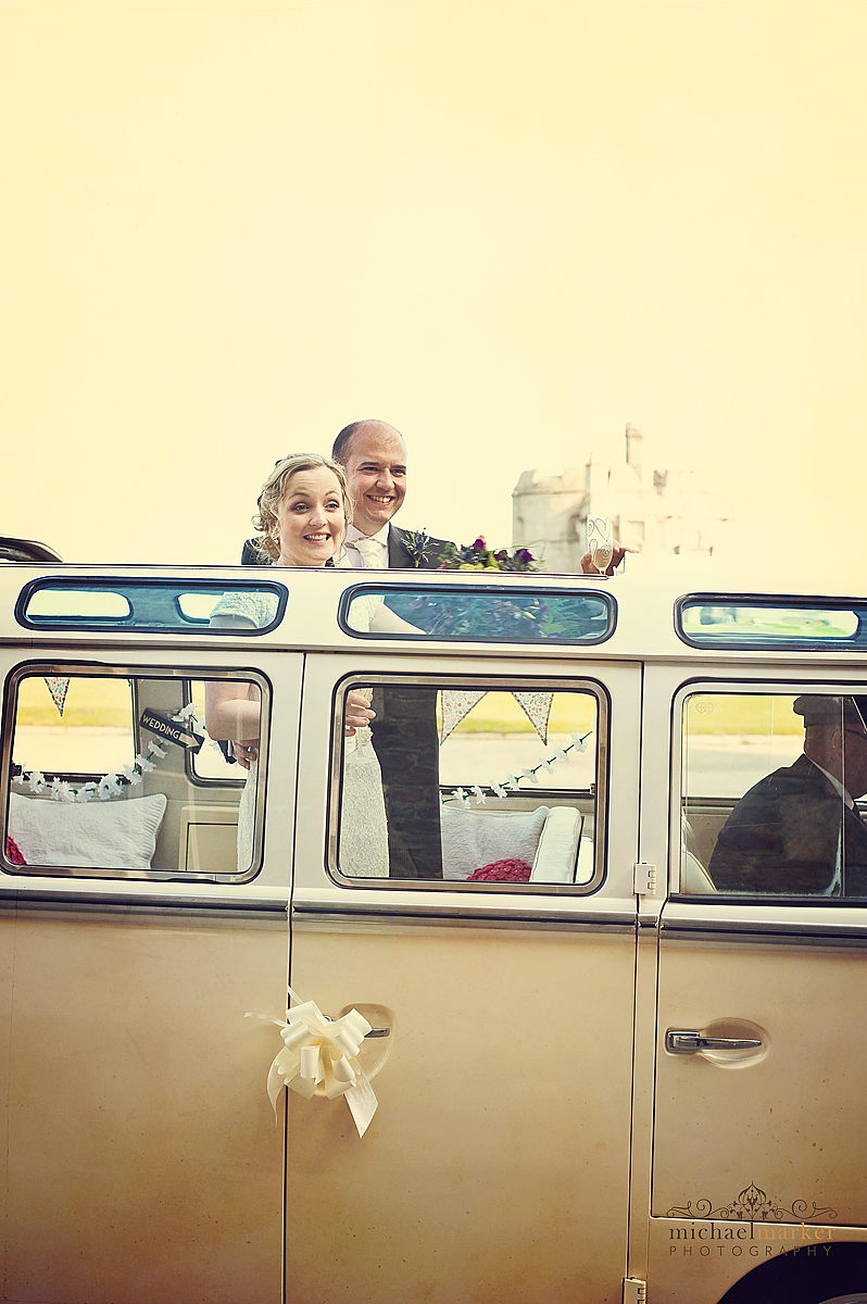 Cornwall wedding in Falmouth with bride and groom looking out of the roof of a vintage campervan parked in front of Pendennis Castle.