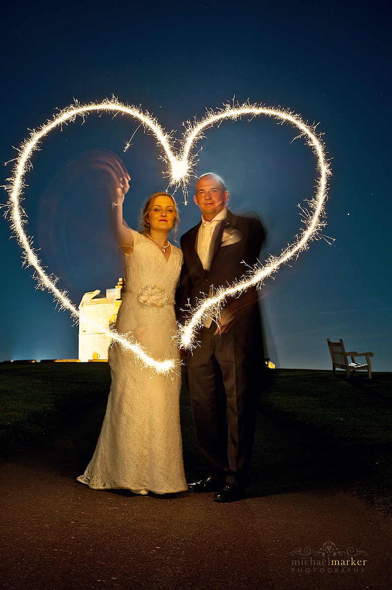 Falmouth wedding bride and groom creating sparkler heart shapes with Pendennis Castle in the background