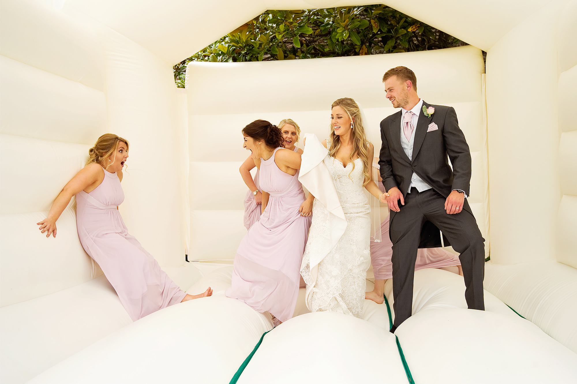 Bride and groom and bridesmaids having fun on a bouncy castle at Langdon Court