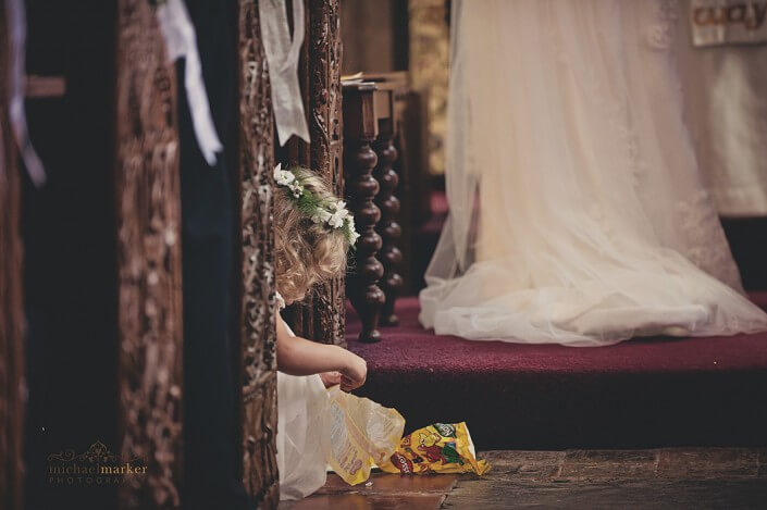 Flowergirl seated on floor of the church eats sweets from a bag during the wedding service near Bideford in North Devon.