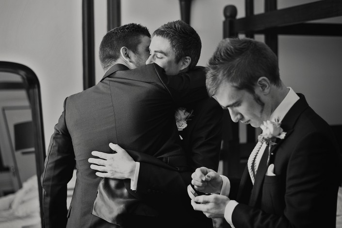 Black and white photos of Bestman checking the wedding rings whilst the groom embraces one of his groomsmen in the background.