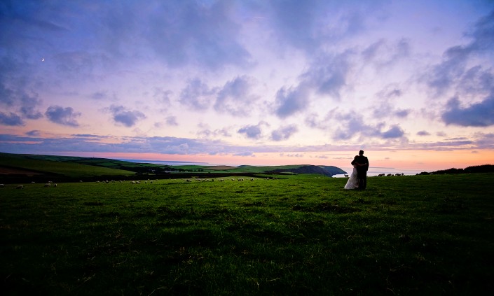 Bride and groom looking over the Atlantic Ocean in North Devon at sunset