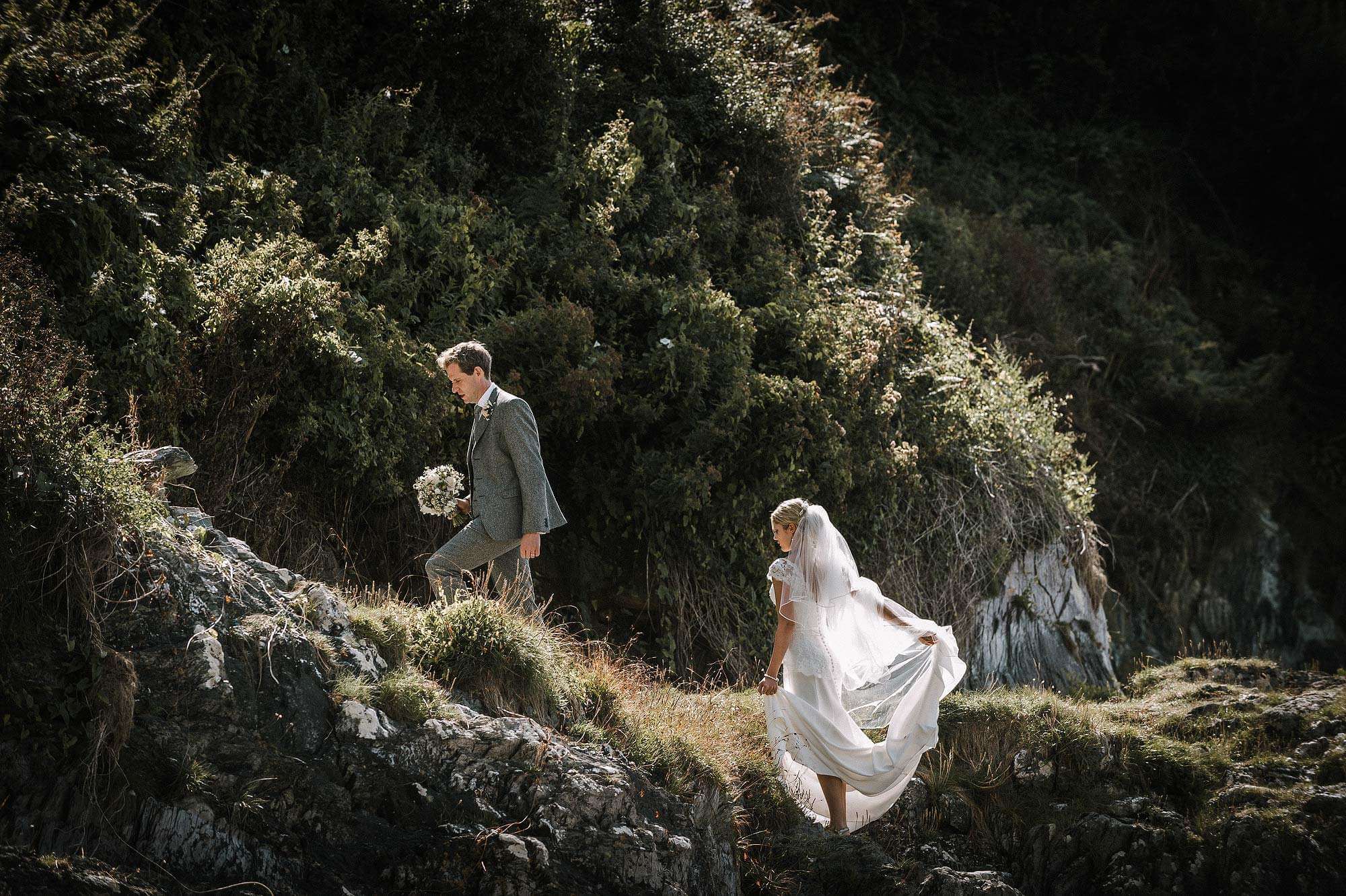 Vintage Bride and groom walk up from the beach at polhawn Fort in cornwall