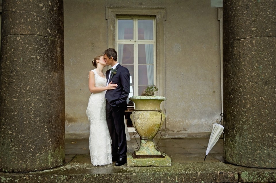 Bride and groom kiss on terrace of North Devon country house on their wedding day.