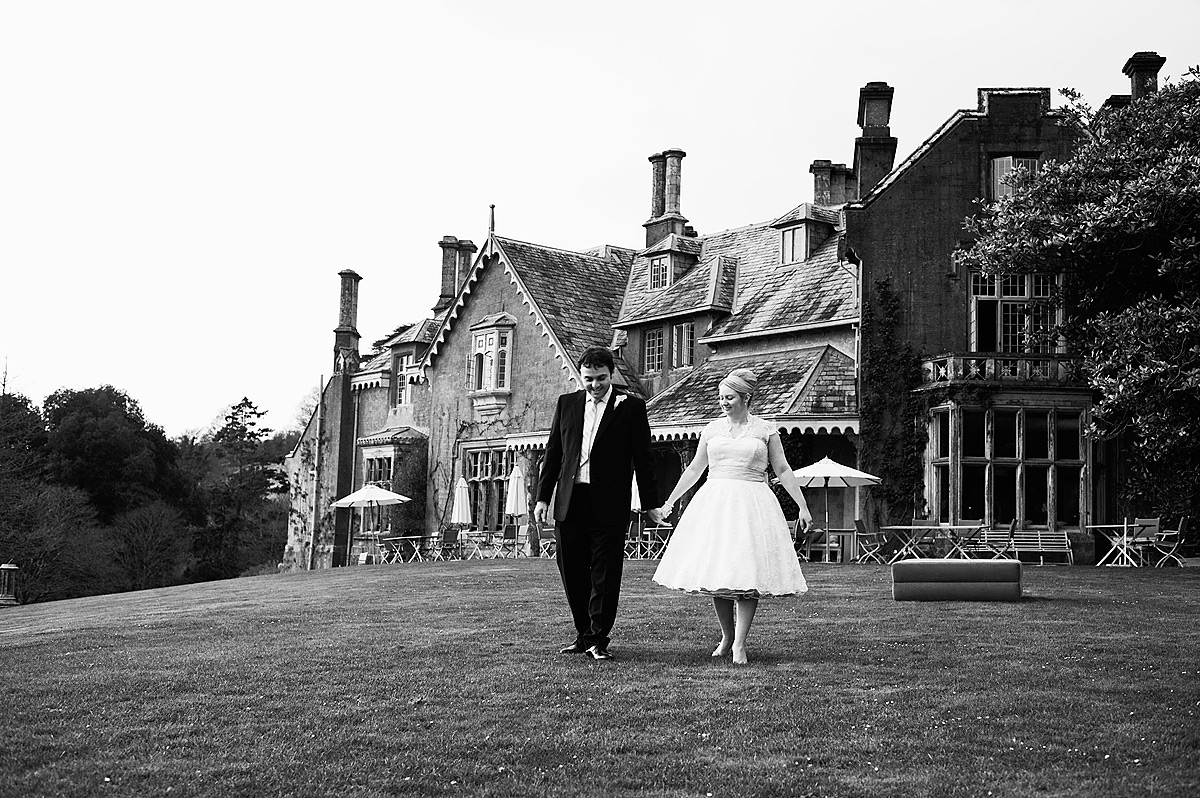 Black and white photo of bride and groom walking front of Hotel Endsleigh in Devon