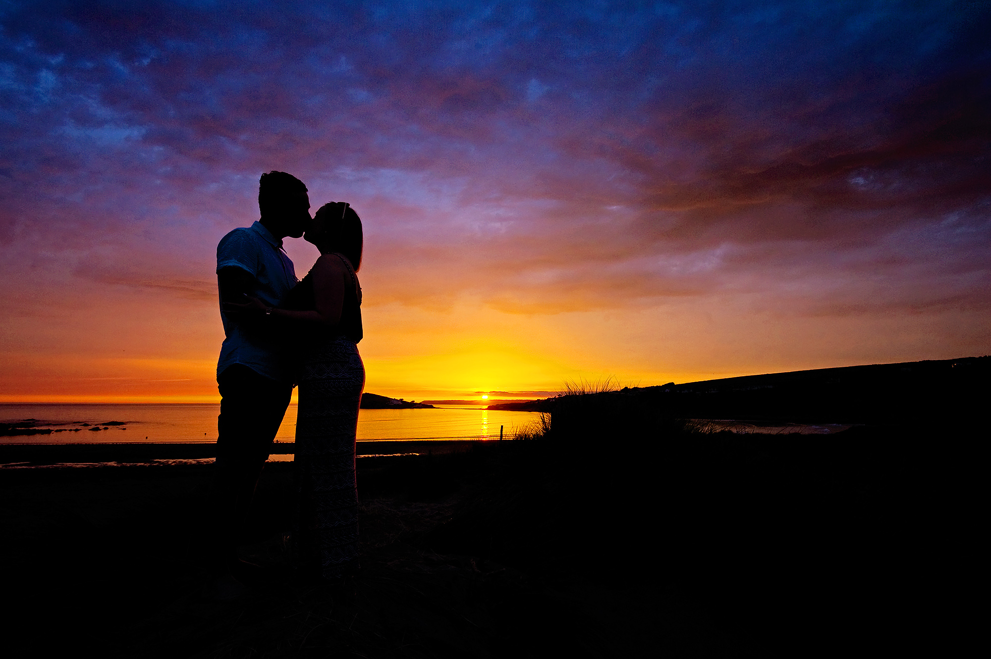 Engaged couple kissing at sunset on Bigbury beach in devon