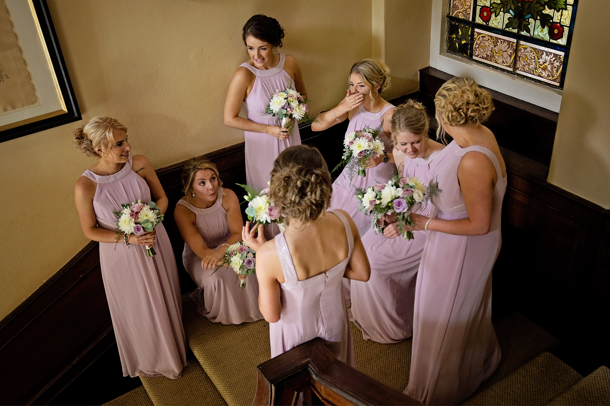 Bridesmaids in pink dresses waiting on the stairs at Langdon Court