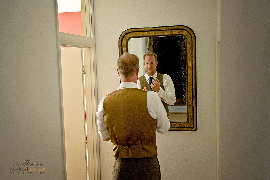 groom tieing his tie in front of mirror