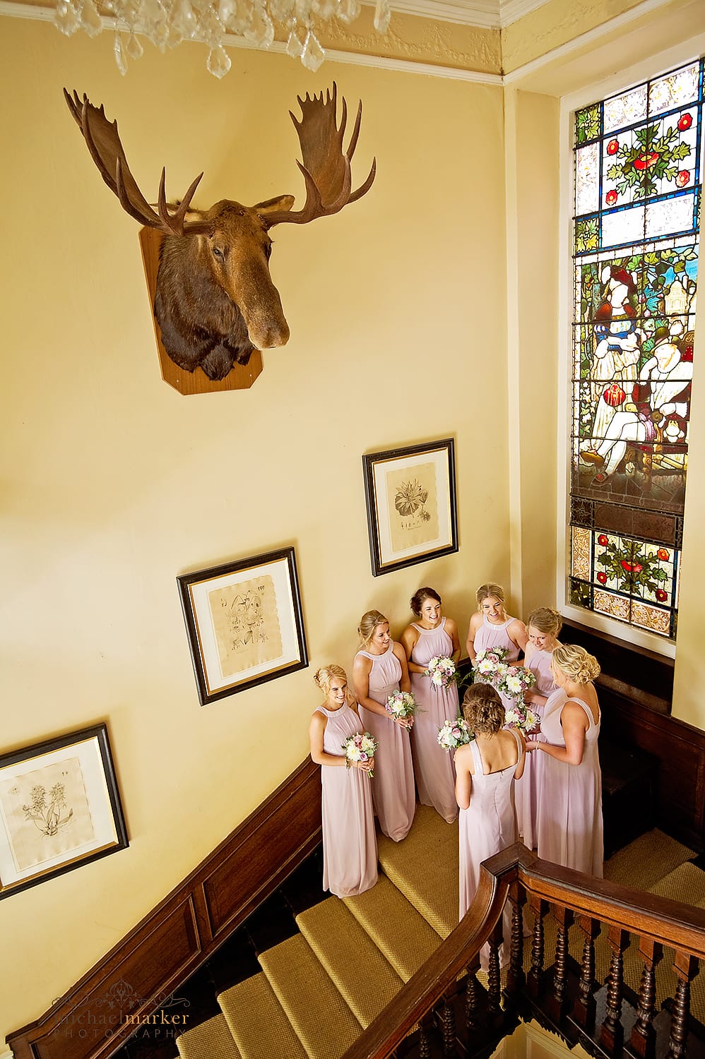 Bridesmaids waiting on the main staircase of Langdon Court under a taxidermy moose head.