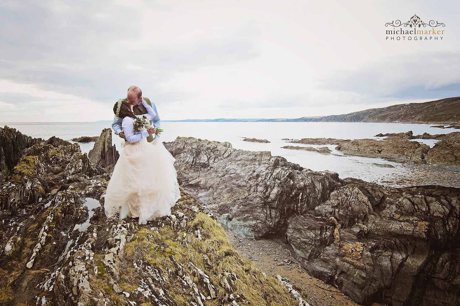 Bride and groom kiss on rocks at Cornish beach wedding