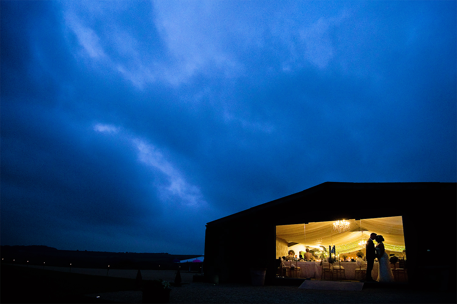 Bride and groom silhouetted in window of Axnoller Farm wedding reception barn at dusk