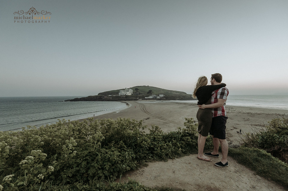 Engaged couple embracing looking towards Burgh Island from Bigbury beach top