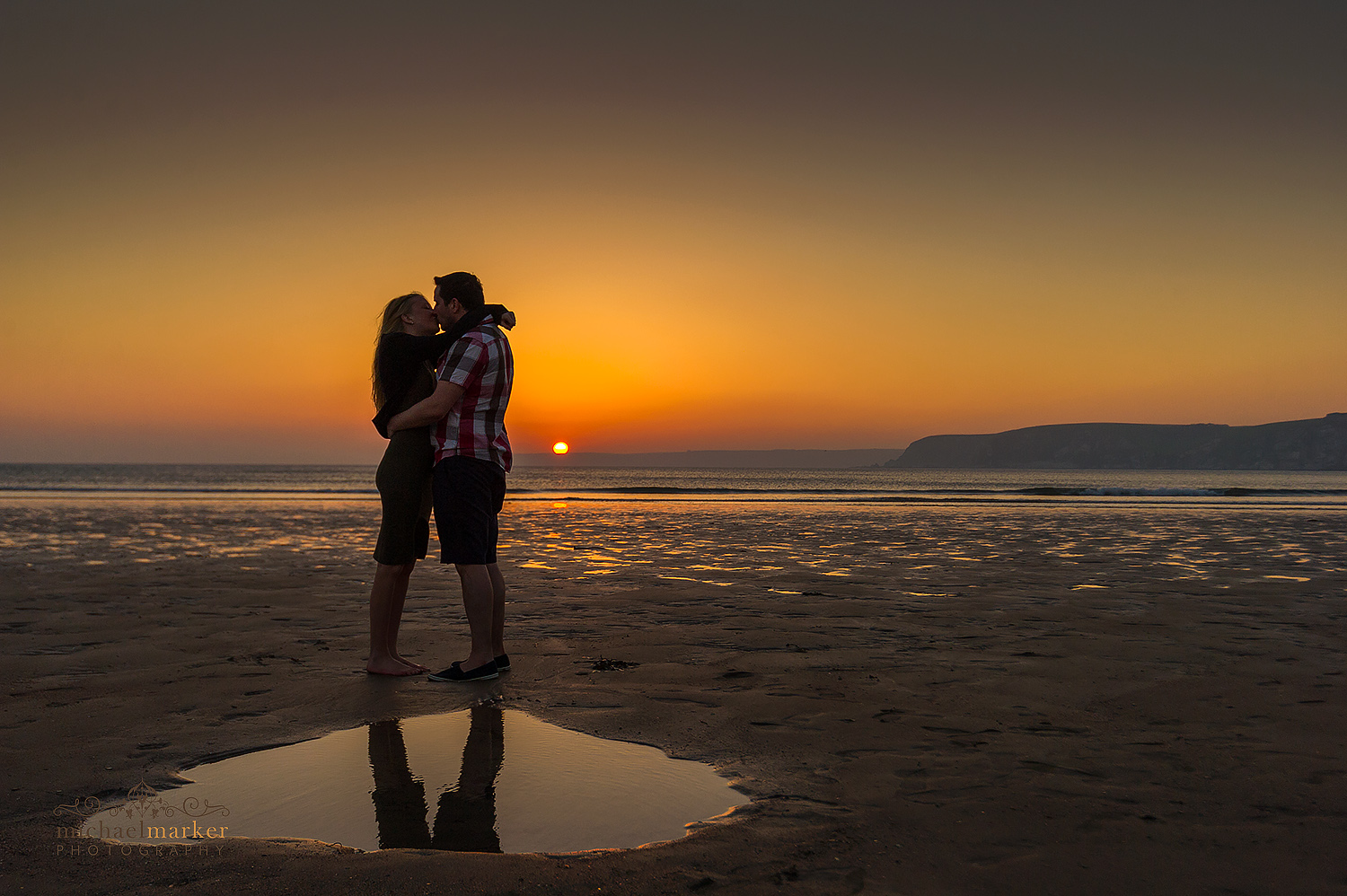 Engaged couple kiss at sunset with Burgh Island in Devon behind