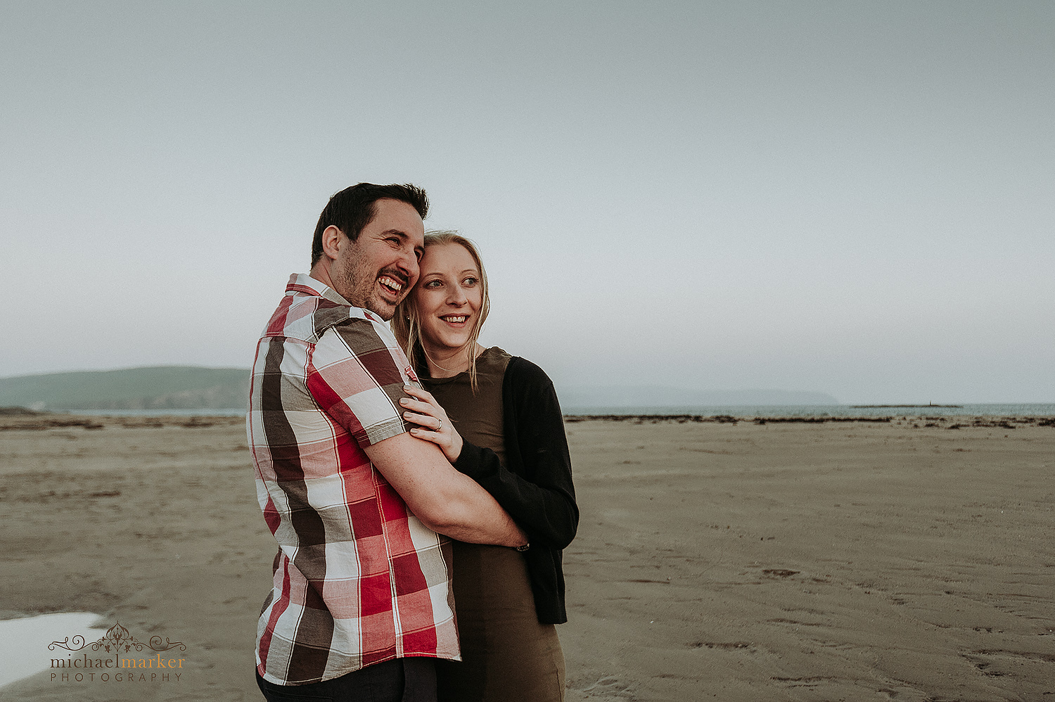 engaged couple on beach embrace and laughing