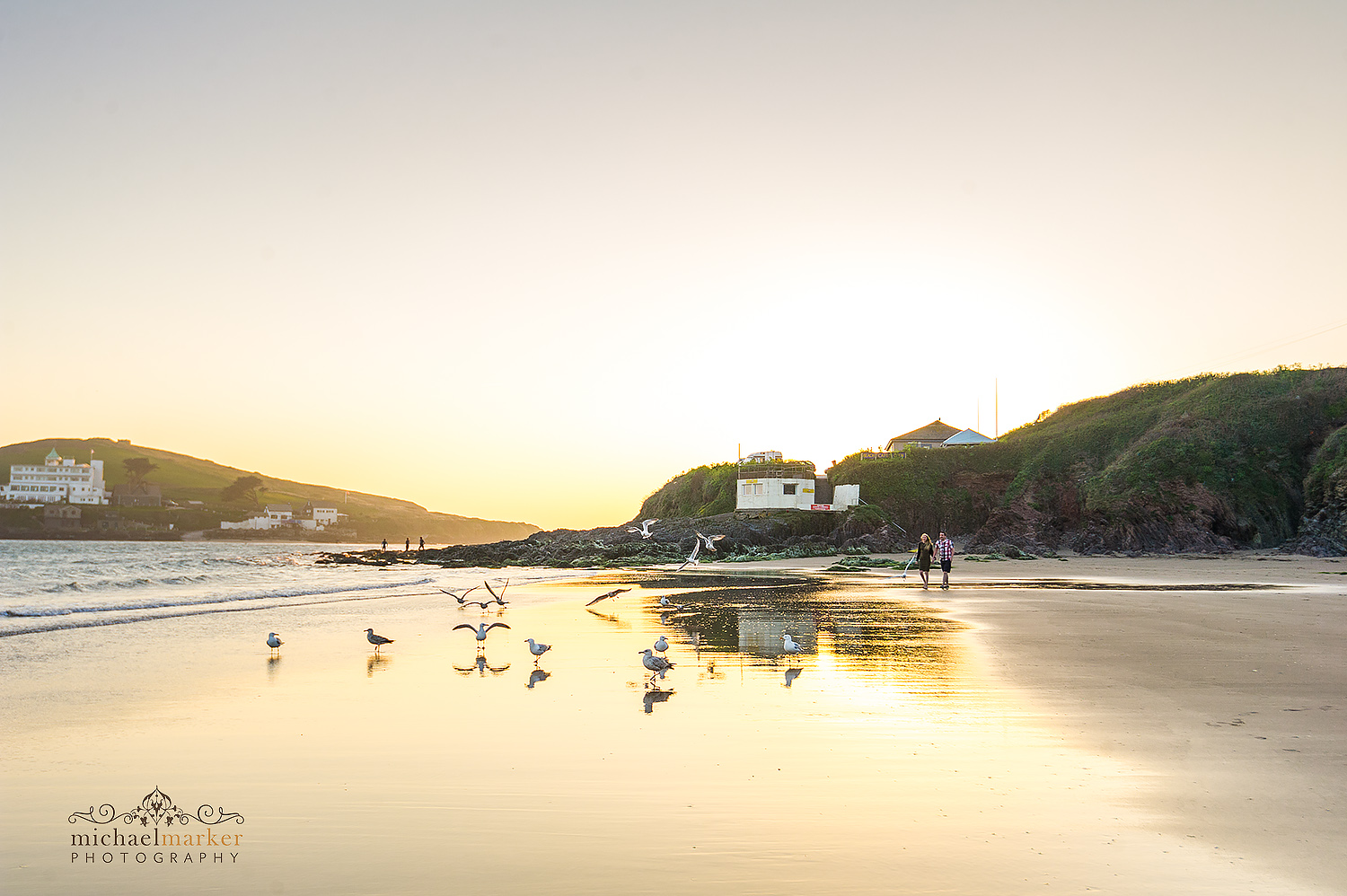 Couple walking along Bigbury beach at sunset