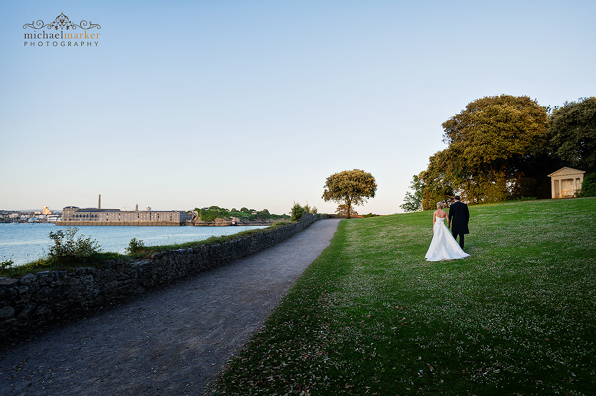 Wedding couple walk beside the Tamar River with the Royal William Yard in the background.