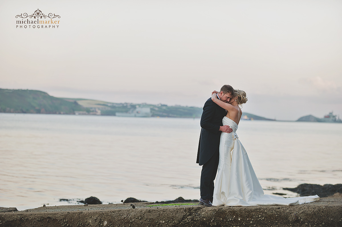 Plymouth weddign couple embrace by the waterfront with the Plymouth Sound in the background.