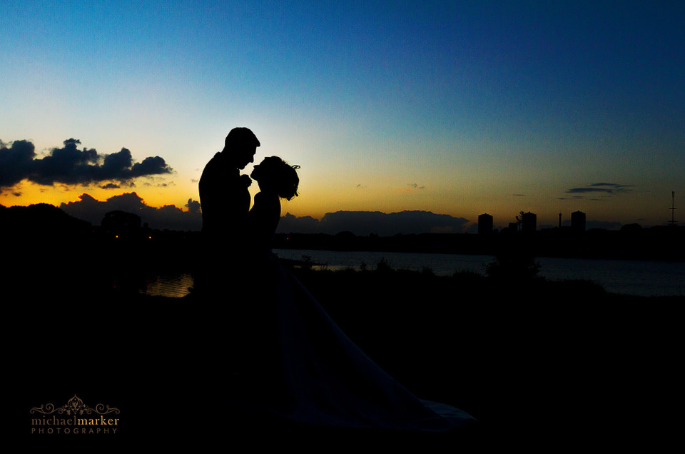 Bride and groom silhouette at sunset on the River Tamar. Colourful sky.