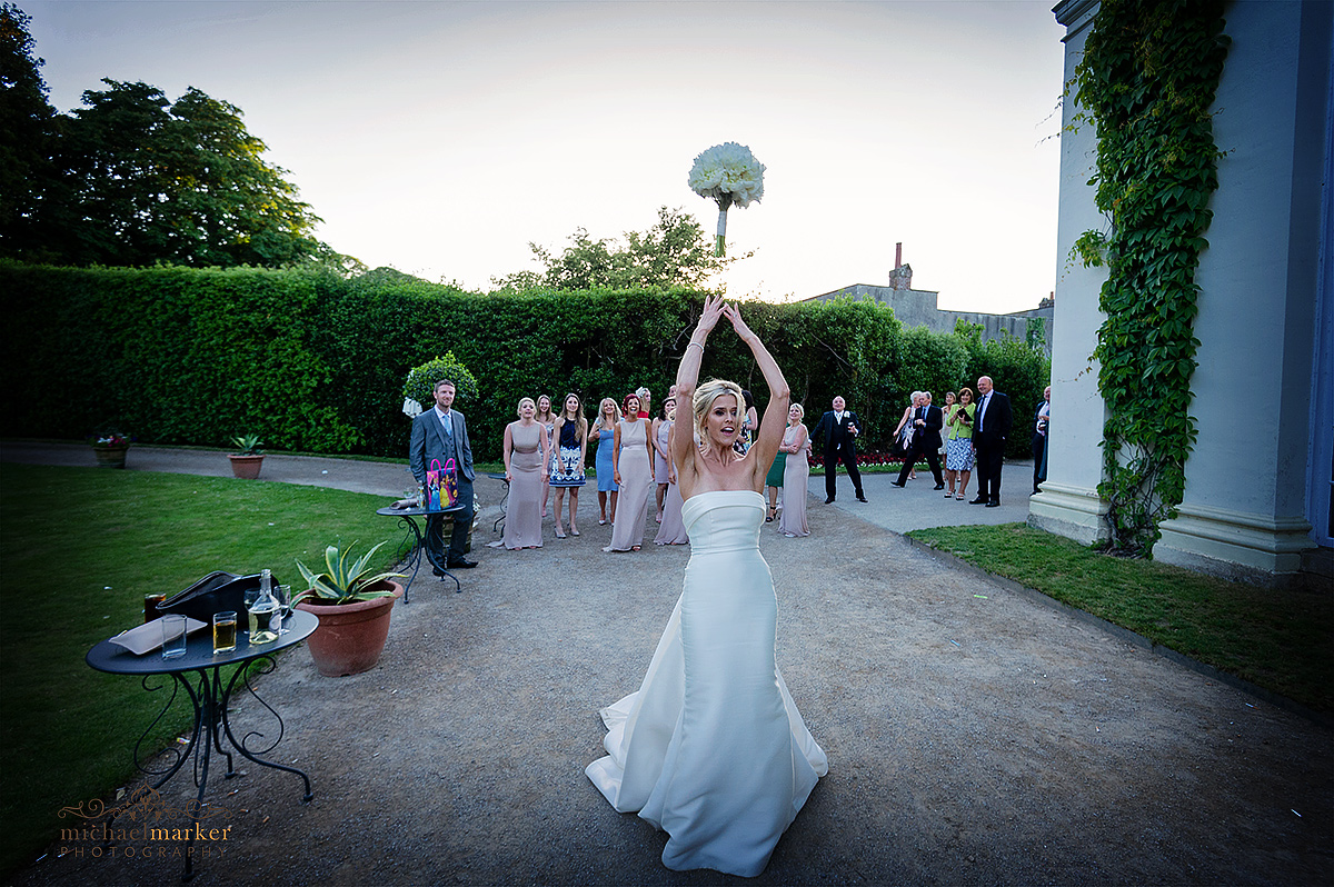 Bride throwing the wedding bouquet as women guests wait to catch it outside Mount Edgcumbe Orangery