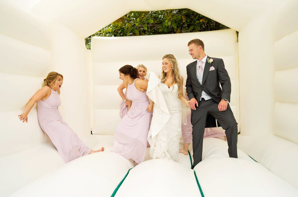 Bride and groom and bridesmaids having fun on a bouncy castle at Langdon Court