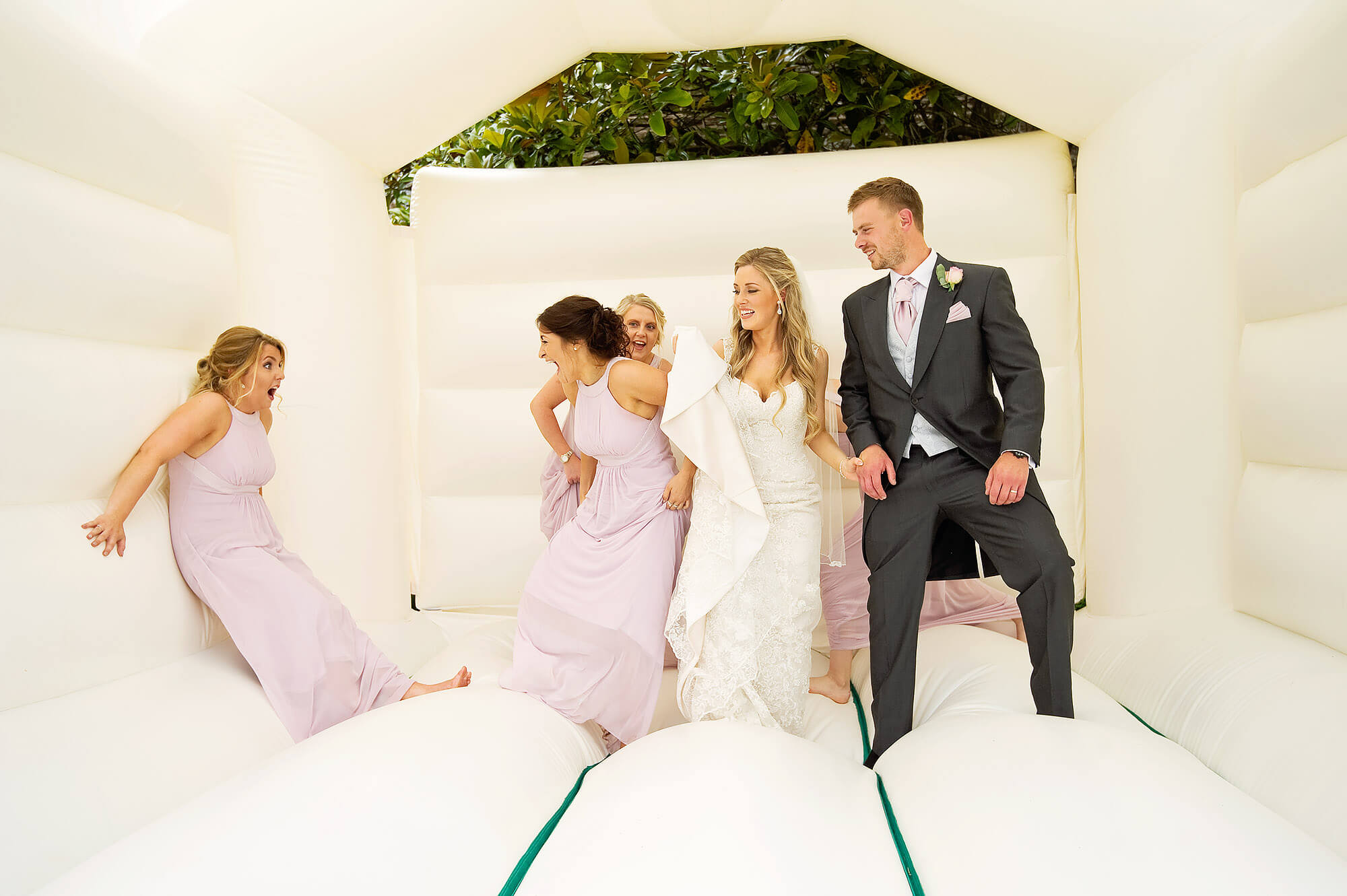 Bride and groom and bridesmaids having fun on a bouncy castle at Langdon Court