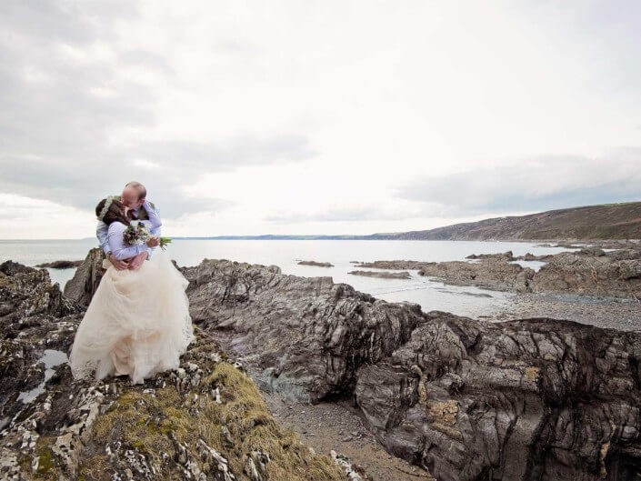 Bride and groom kiss on rocks at Cornish beach wedding at Polhawn Fort.