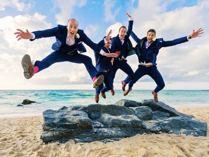Groom and three groomsmen jumping for joy off rocks on Porthmeor Beach in St Ives Cornwall.