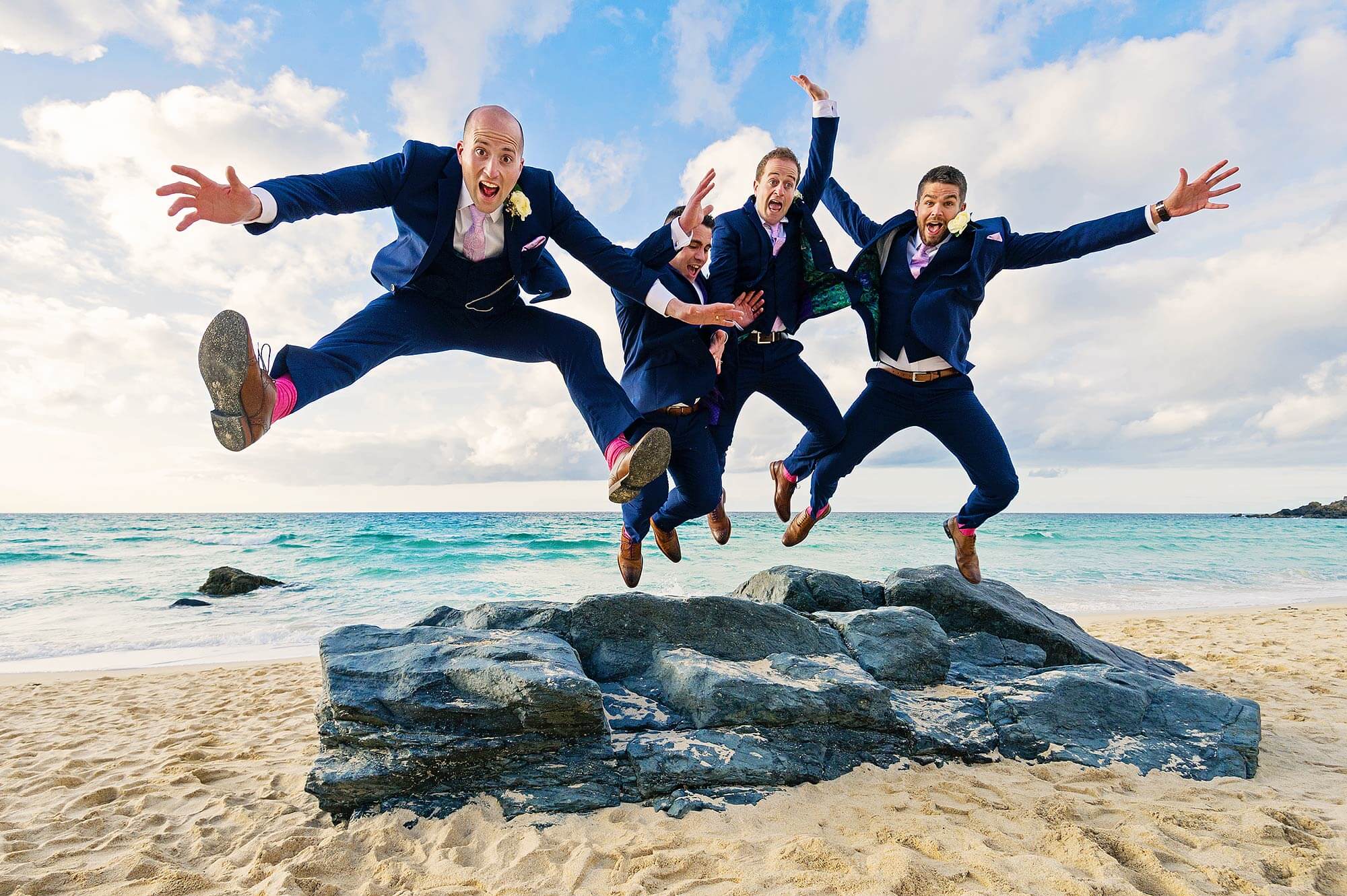 Groom and three groomsmen jumping for joy off rocks on Porthmeor Beach in St Ives Cornwall.