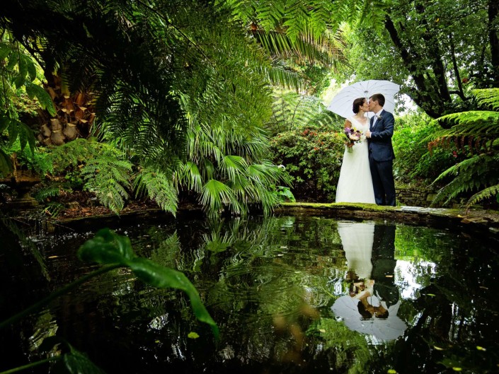 Bride and groom kiss in front of the tropical garden pond at Lamorran House Gardens in St Mawes Cornwall.