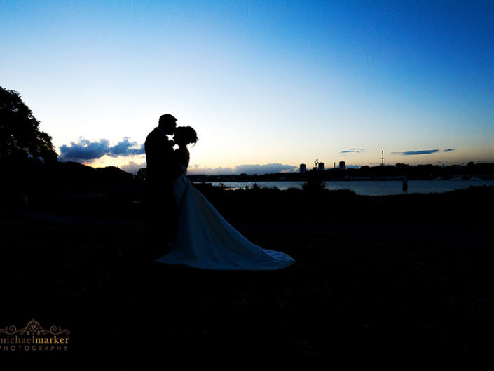 Bride and groom tender kiss at Mount edcumbe wedding at sunset overlooking Plymouth skyline.