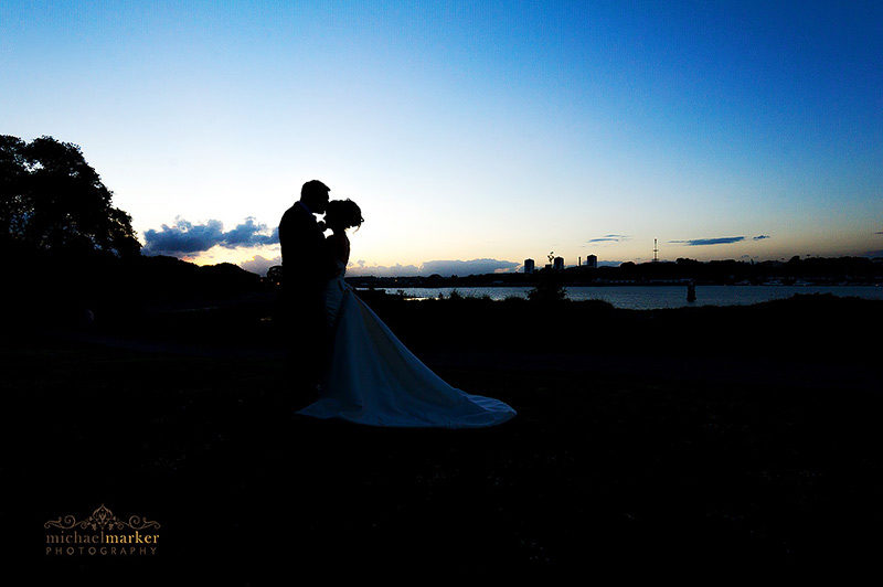 Bride and groom tender kiss at Mount Edgcumbe wedding at sunset overlooking Plymouth skyline.