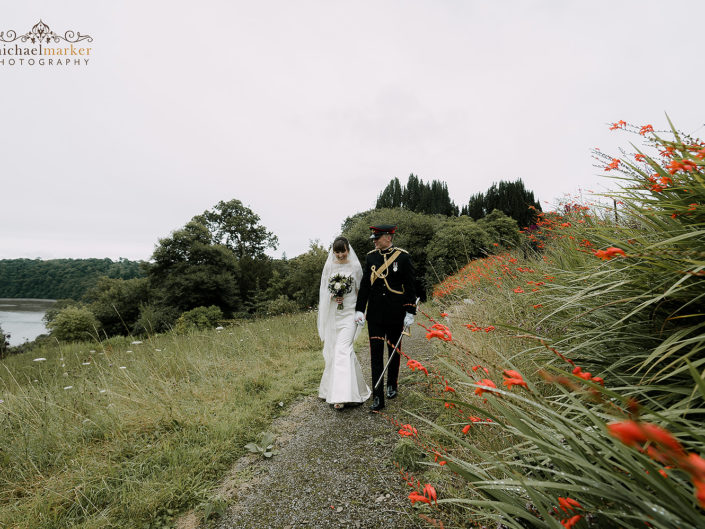 Bride and Army officer husband walk in gardens of Pentillie Castle overlooking the river Tamar on their wedding day.