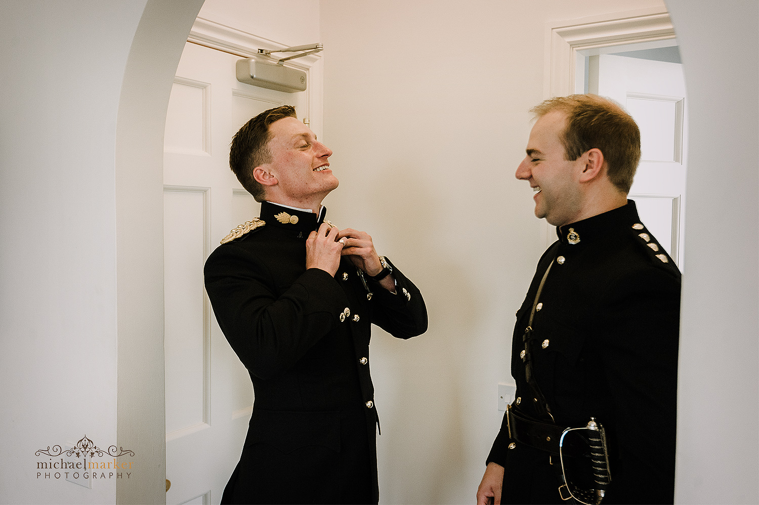 Military officer wedding groom getting dressed with help of his bestman at Pentillie Castle in Cornwall.