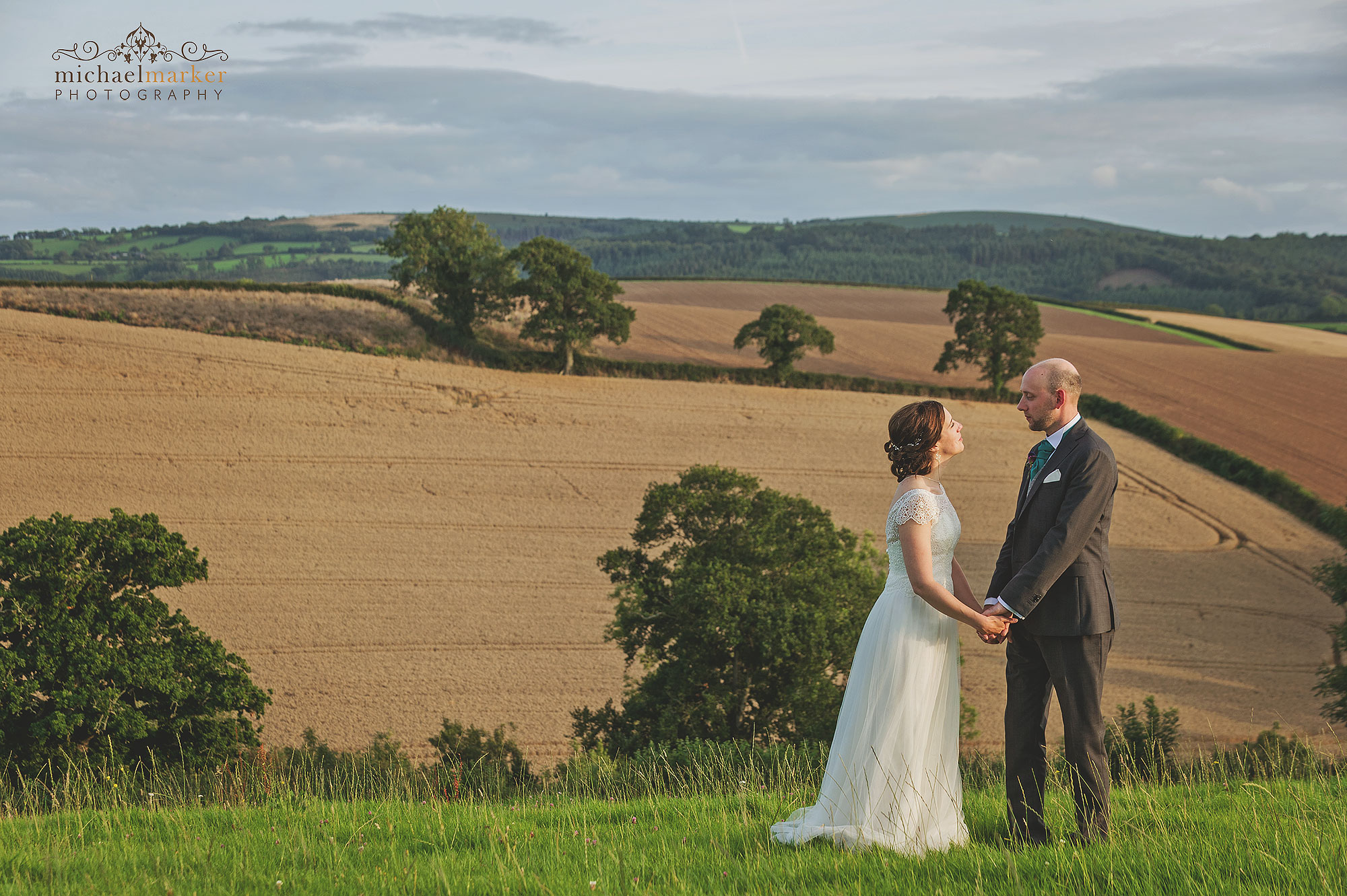 Bride and groom hold hands and look at each other in field at Higher Egbbeer in devon.