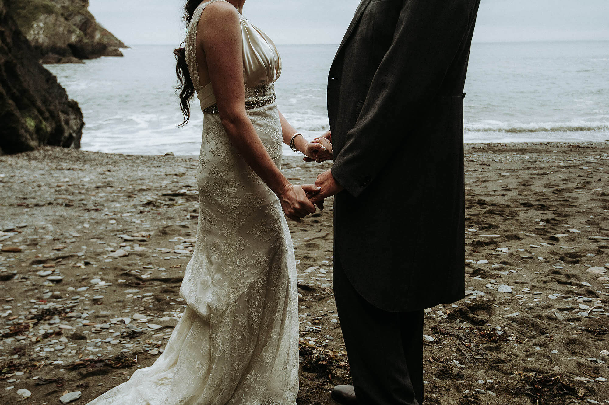 Wedding day couple holding hands on secluded North Devon beach