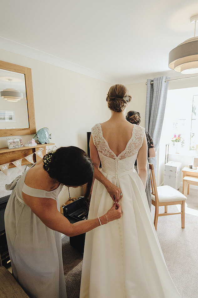 Bridesmaid buttoning the back of the wedding dress before the Devon wedding at Shilstone