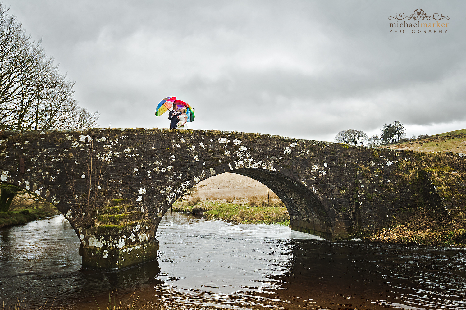 Bride and groom and colourful umbrellas on bridge at Two Bridges Hotel on Dartmoor.