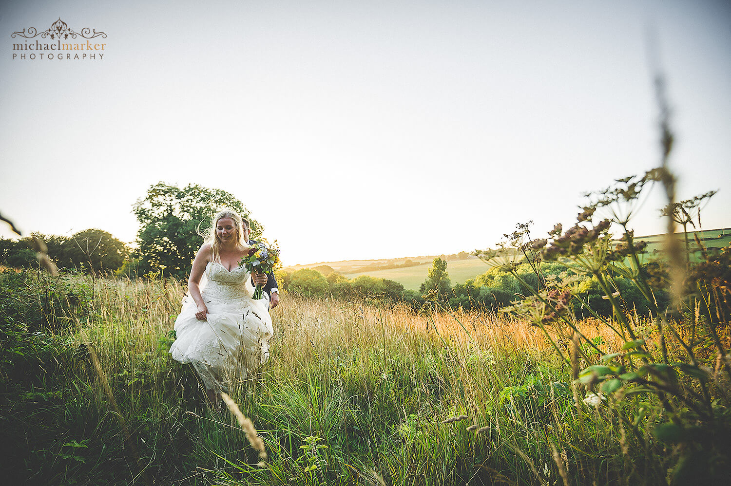 Bride and groom walk through flower meadow field back to wedding reception at Trevenna